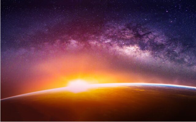 Digitally rendered image of sun emerging over Earth's horizon, light breaking and Milky Way galaxy in background. Image created digitally based on elements furnished by NASA.