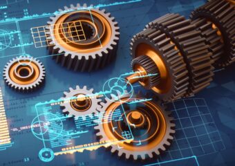 Engineering blueprints of a mechanism's design with computer coding and machine components placed on top of the blueprints.