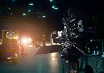 Movie camera on set in a studio as production tasks are happening in the background.