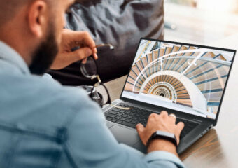 Male freelancer holds his glasses in his left hand while working on his Dell Latitude 15 9000 series laptop.