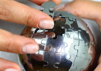 Close up image of a person holding a three dimensional puzzle of Earth in silver, putting in a piece.