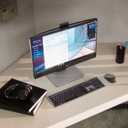 Dell Optiplex 7400 AIO thin client on desk with keyboard, mouse, headphones and writing notebook.