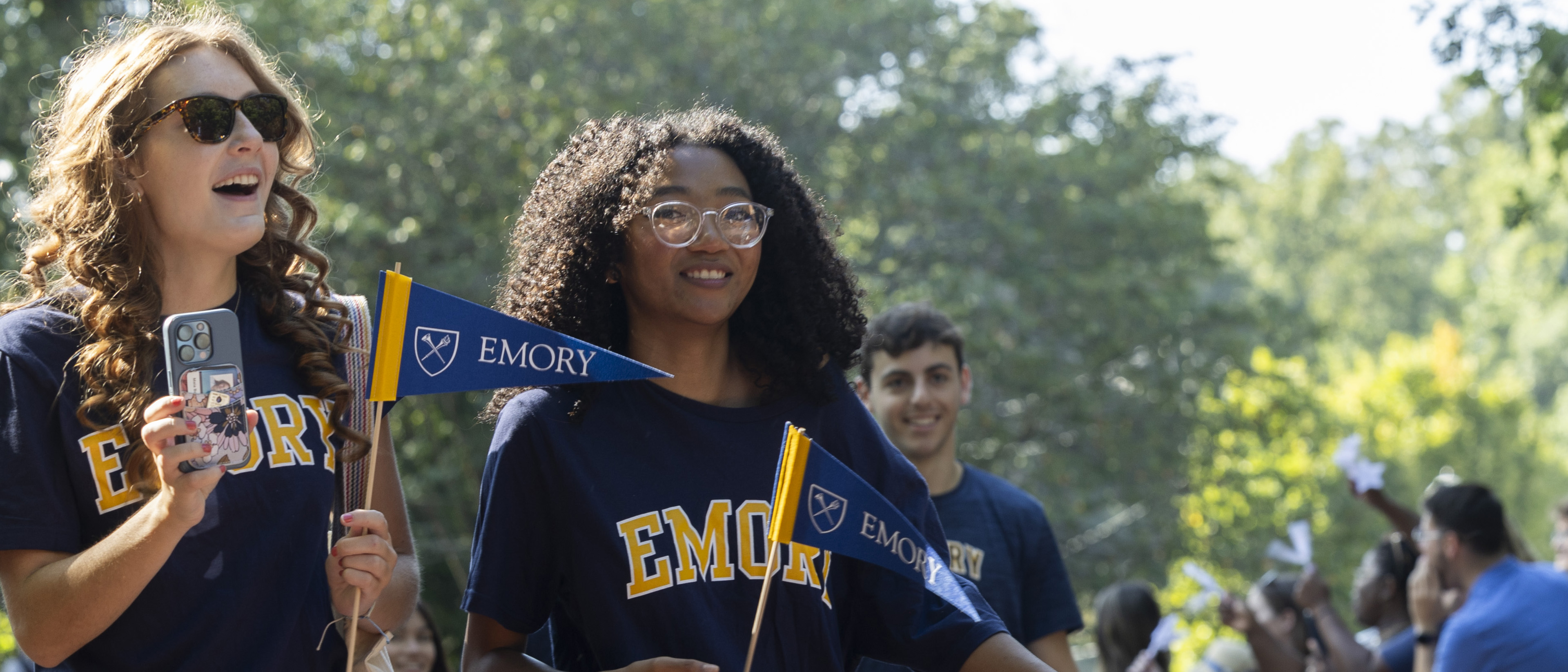 Students wearing Emory t-shirts and waving Emory pennants walk through the university's main gate during first-year orientation