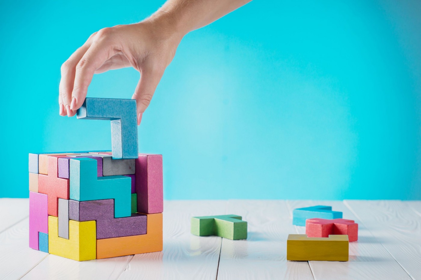 A cube puzzle game being constructed by a person's hand on a table