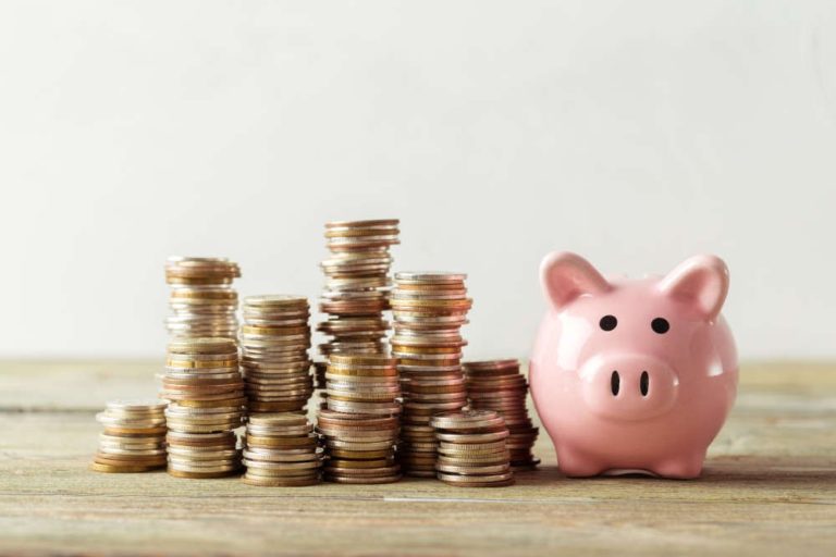 Stack of coins next to a piggy bank on a table