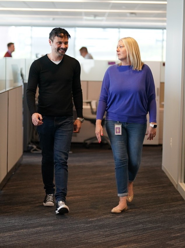 Two ensono employees, a man and a woman, walking and talking in an office