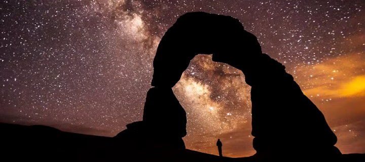 Silhouette of person and rock formation in front of sky full of stars