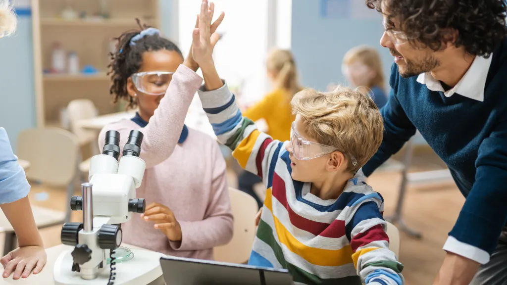 Two kids giving each other a high five in an elementary science classroom.