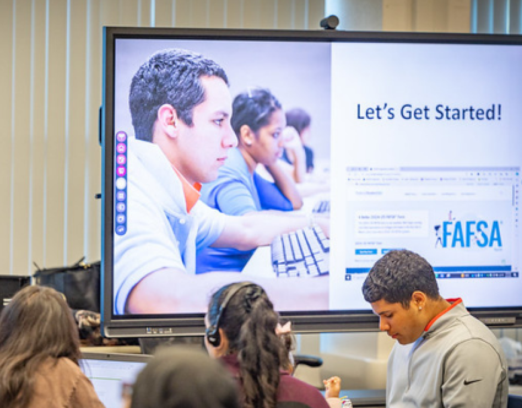 A group of students sitting in front of a projection screen that reads "Let's Get Started" and "FAFSA."