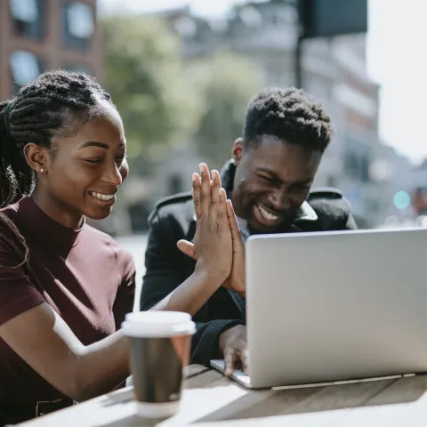 Two African American students working on a computer and giving each other high fives.