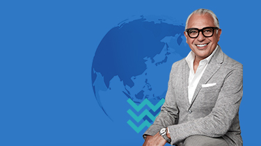 Joe Mimran poses with globe with blue chevrons in background.