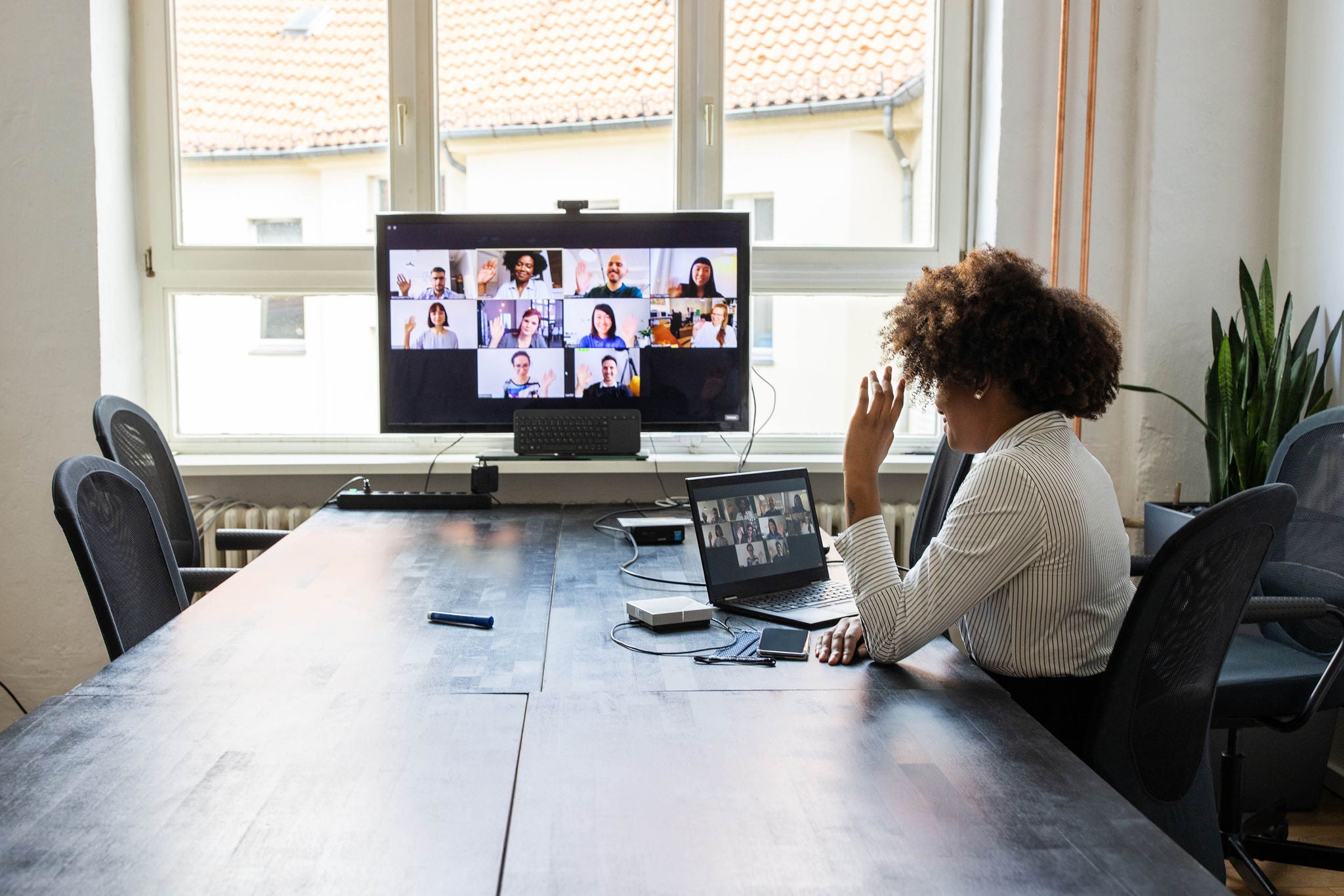 Rear view of a businesswoman having a meeting with team over a video conference in office board room. Meeting over a video call in office post pandemic lockdown.