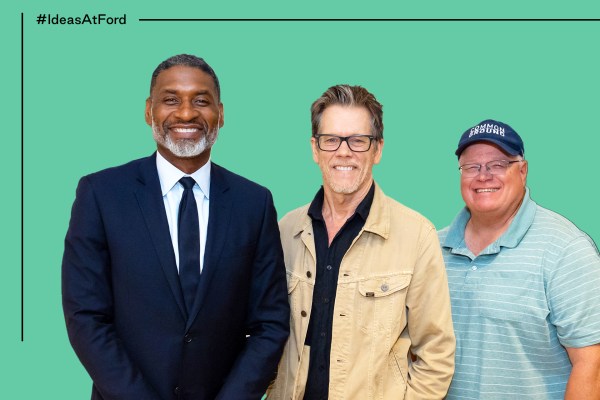 Three men stand and smile in front of a green background. Charles Blow, the first man on the left, wears a dark suit and tie. The middle man, Kevin Bacon, is wearing glasses and a beige jacket over a dark shirt. The man on the right, Gabe Brown, is wearing a blue cap and a striped polo shirt. Text in the top left corner reads "#IdeasAtFord."