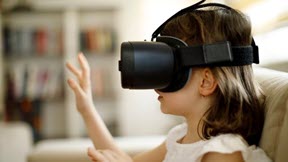 A girl sits down with her hands up and wears a virtual reality headset. 