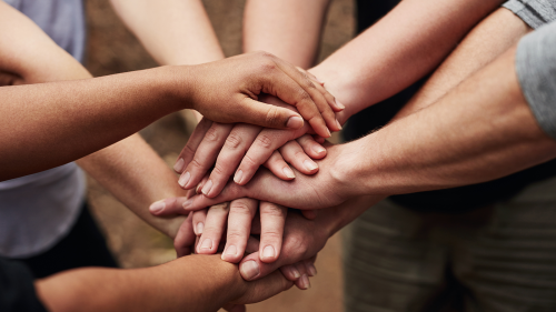 Photo of diverse group of people bringing their hands together.