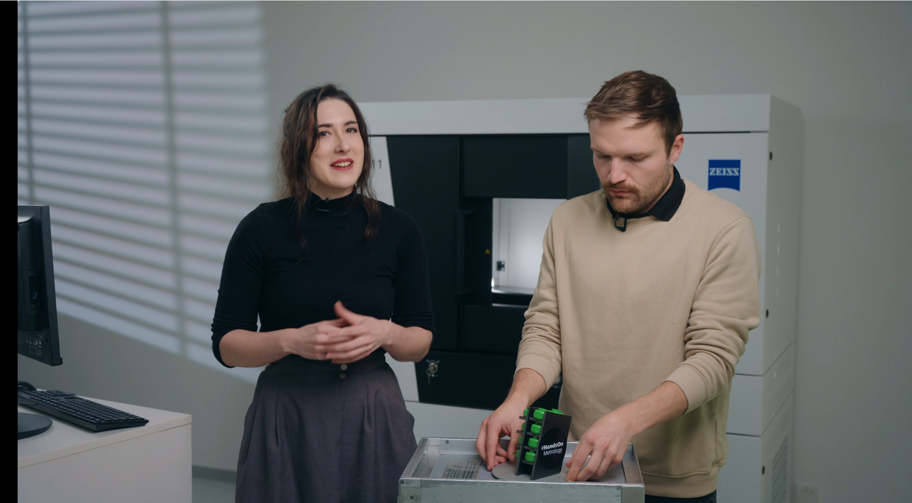 A woman and a man talking about several green plastic parts infront of a CT scanner