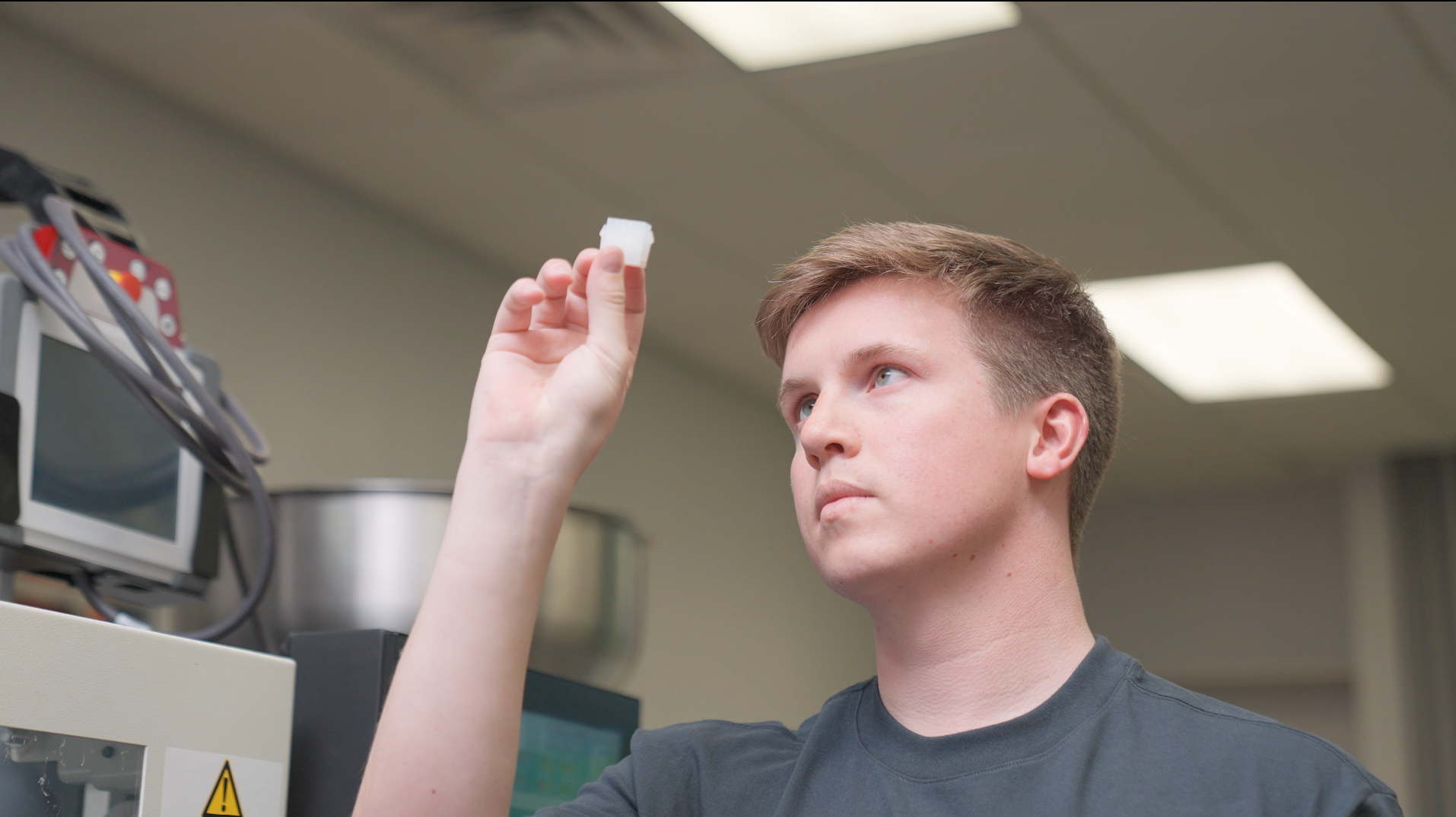 Men holds up a clear plastic part to inspect the object