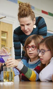 kids and teacher watching kid pour liquid