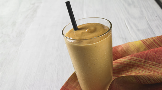 a glass full of pumpkin smoothie, with a drinking straw