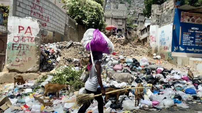 A woman carrying her belongings walks down a street in Port-au-Prince, Haiti. July 2024.