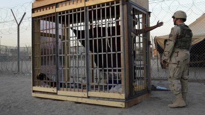 A detainee in an outdoor solitary confinement cell talks with a military police officer at the Abu Ghraib prison on the outskirts of Baghdad, Iraq, June 22, 2004. 