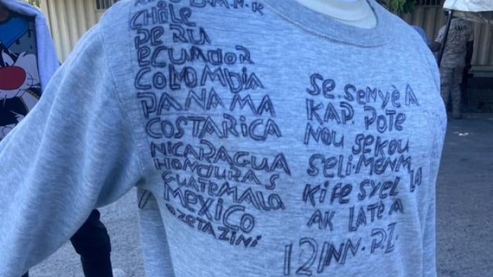 A Haitian who was returned to Haiti from the United States in December 2021 wrote on a sweatshirt the countries he had crossed to get to the US, starting in the Dominican Republic. The writing on the right says, in Creole, “This is the Lord who is rescuing us, he is the one who created heaven and earth.”