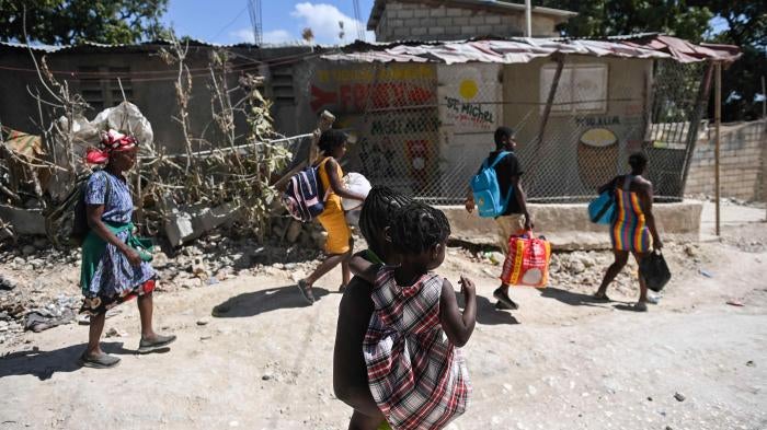 A group of people carry their belongings on a city street 