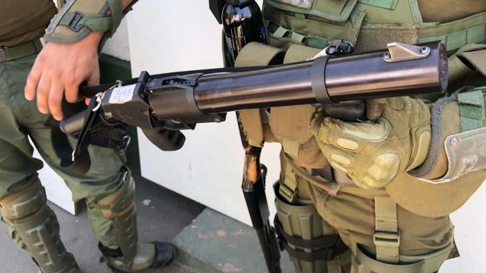 A police captain holds a teargas gun. A pellet shotgun hangs on his right side. 