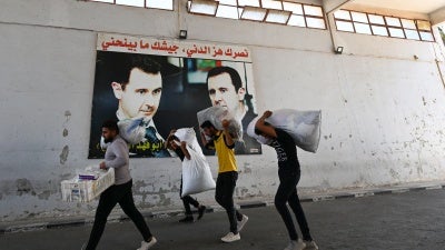 Displaced people walk past posters of President Bashar al-Assad as they enter Syria from Lebanon via the Jusiyeh Border crossing, on October 2, 2024. 