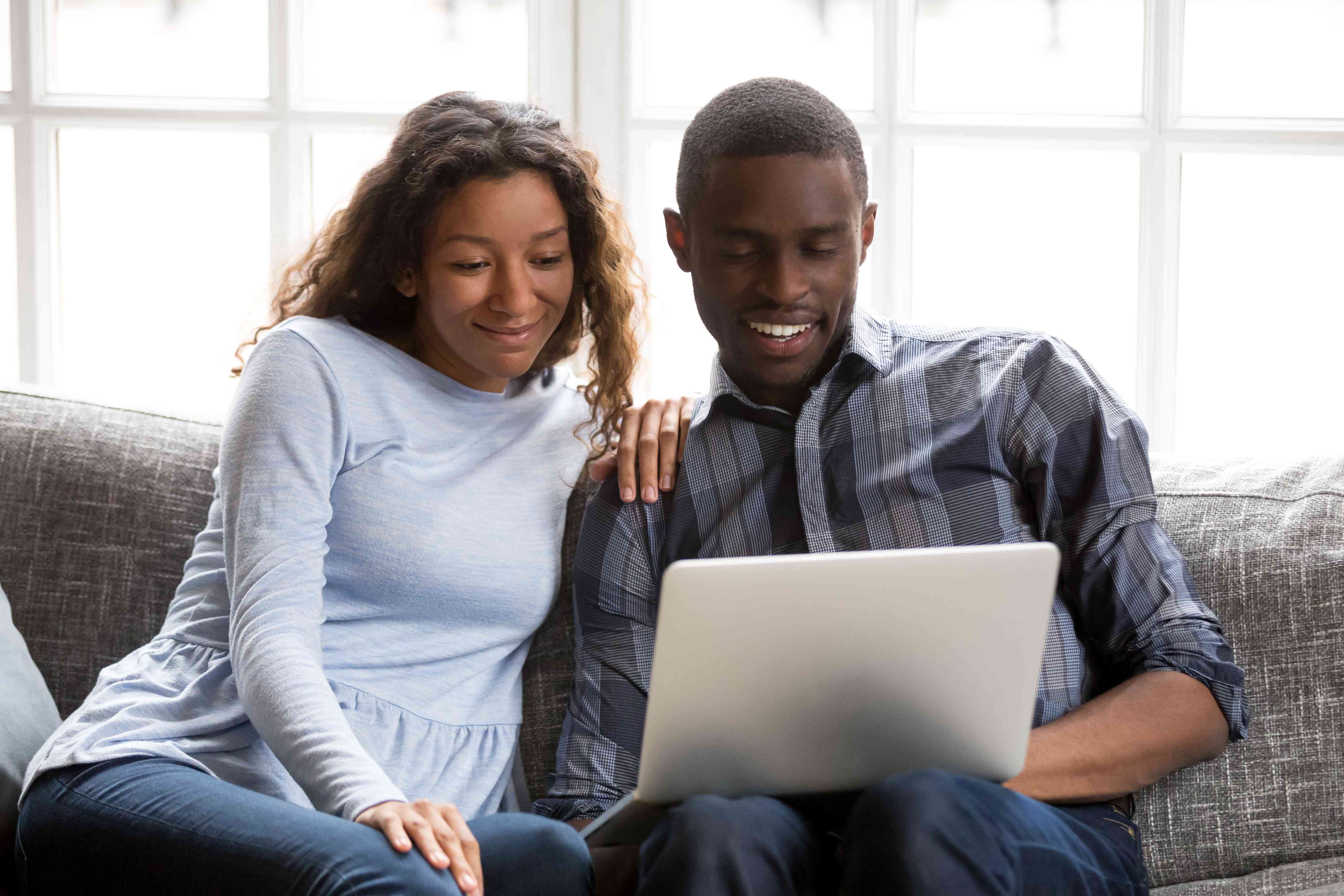 Young couple on their living room couch, looking happily at a laptop together