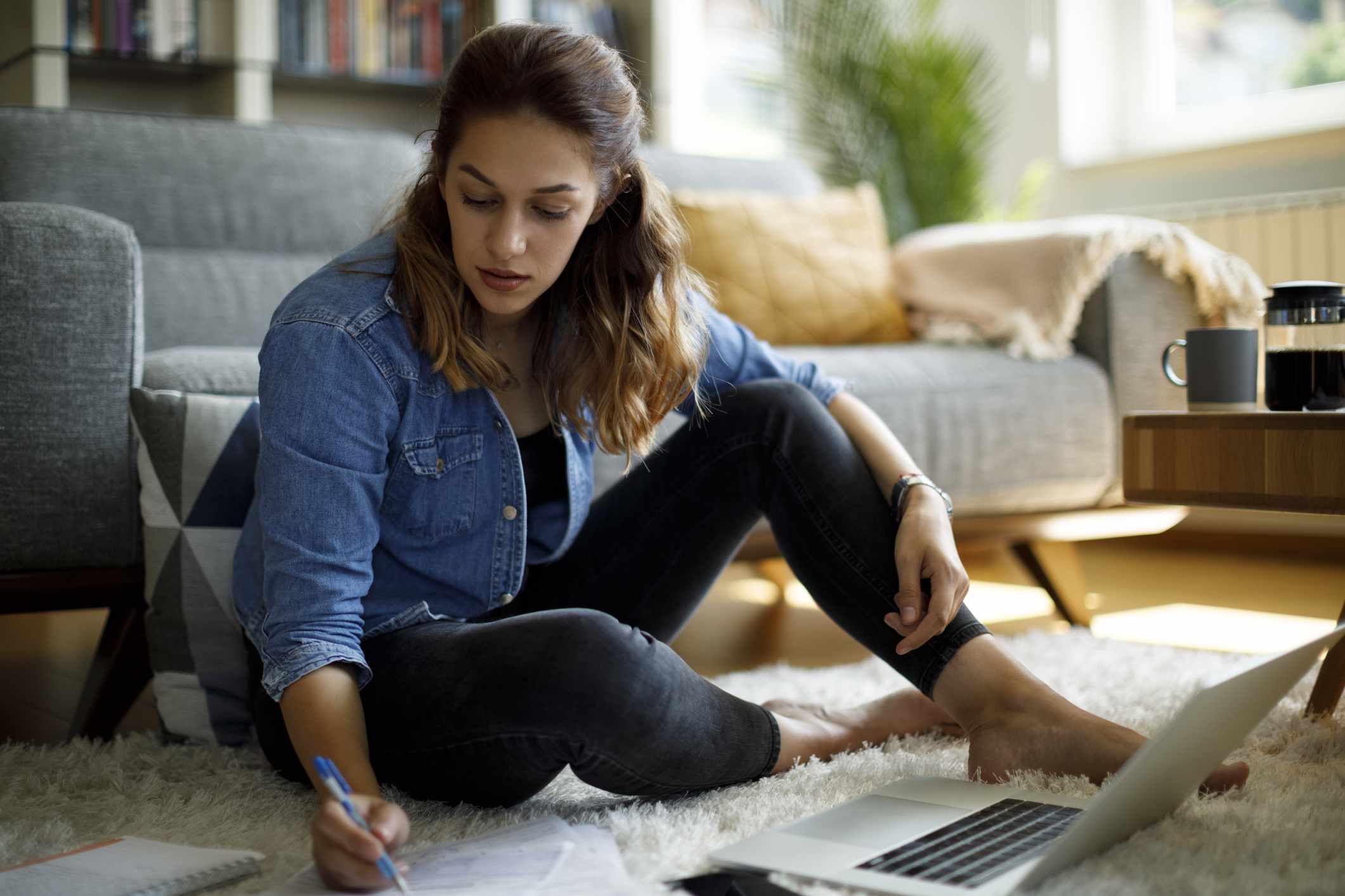 Woman sitting on the floor, checking numbers with a laptop