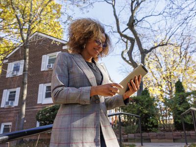 A woman walks down the street looking at a tablet in her hands