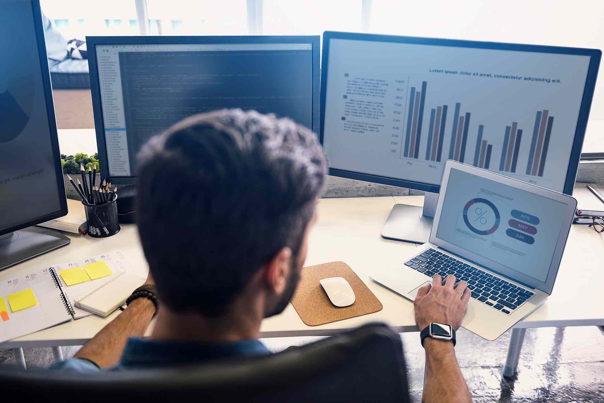 Man working on differents monitors creating statistics in modern office.