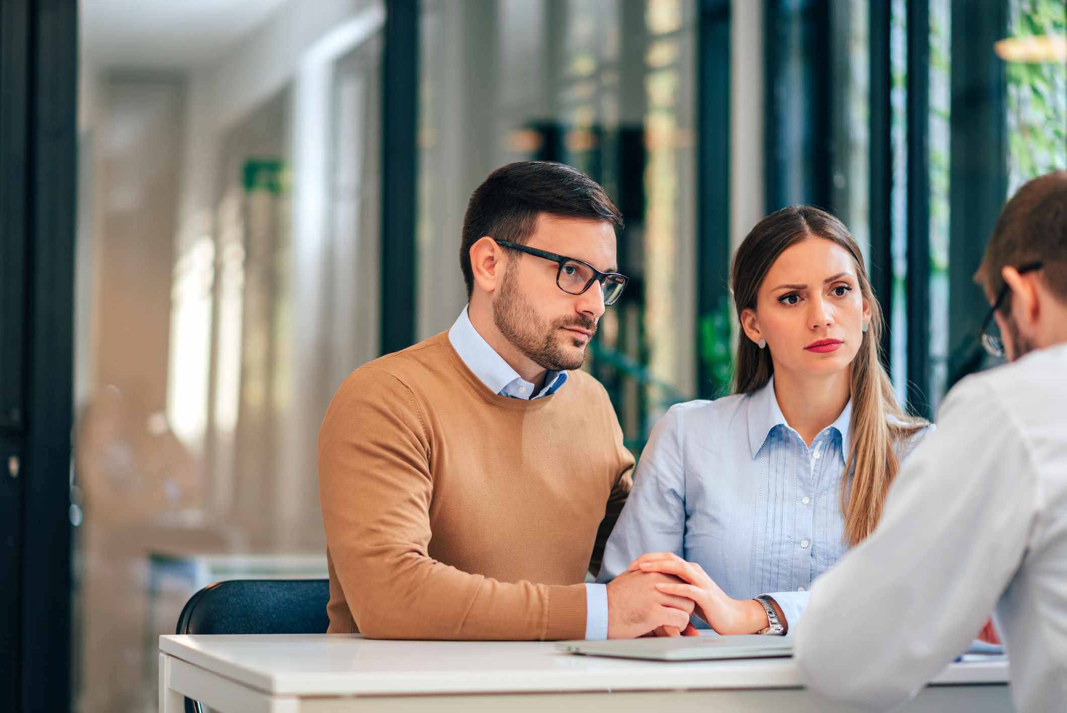 Man and woman holding hands and looking concerned in an office