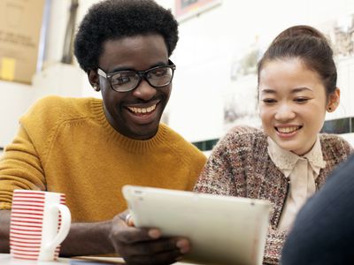 A man and a woman sit looking at a digital tablet, smiling