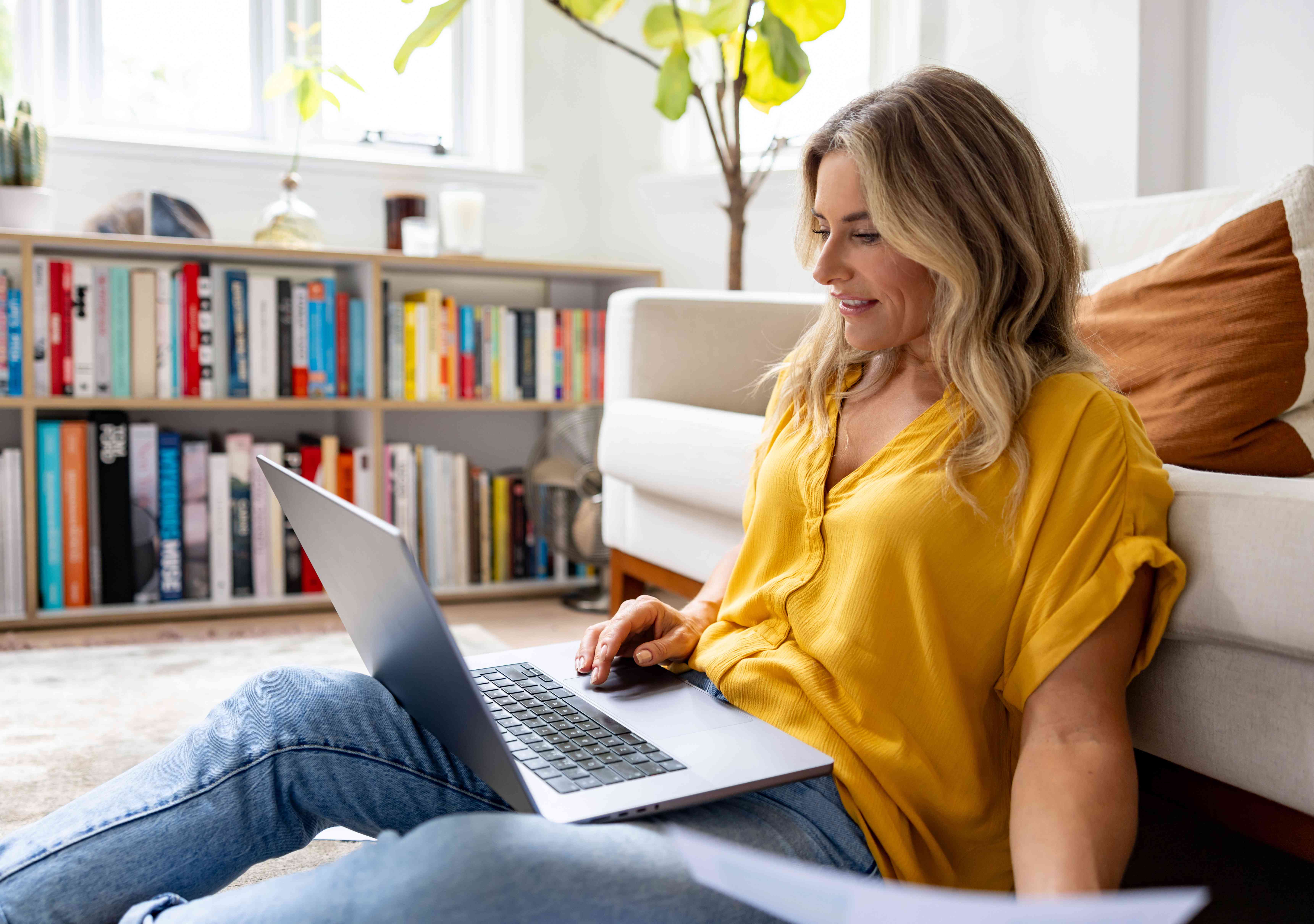 Woman in her 30s sitting on the floor in her living room and looking at her laptop