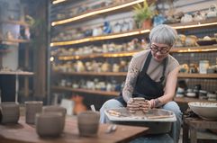 Senior woman artist making clay bowl on a pottery wheel in her studio.