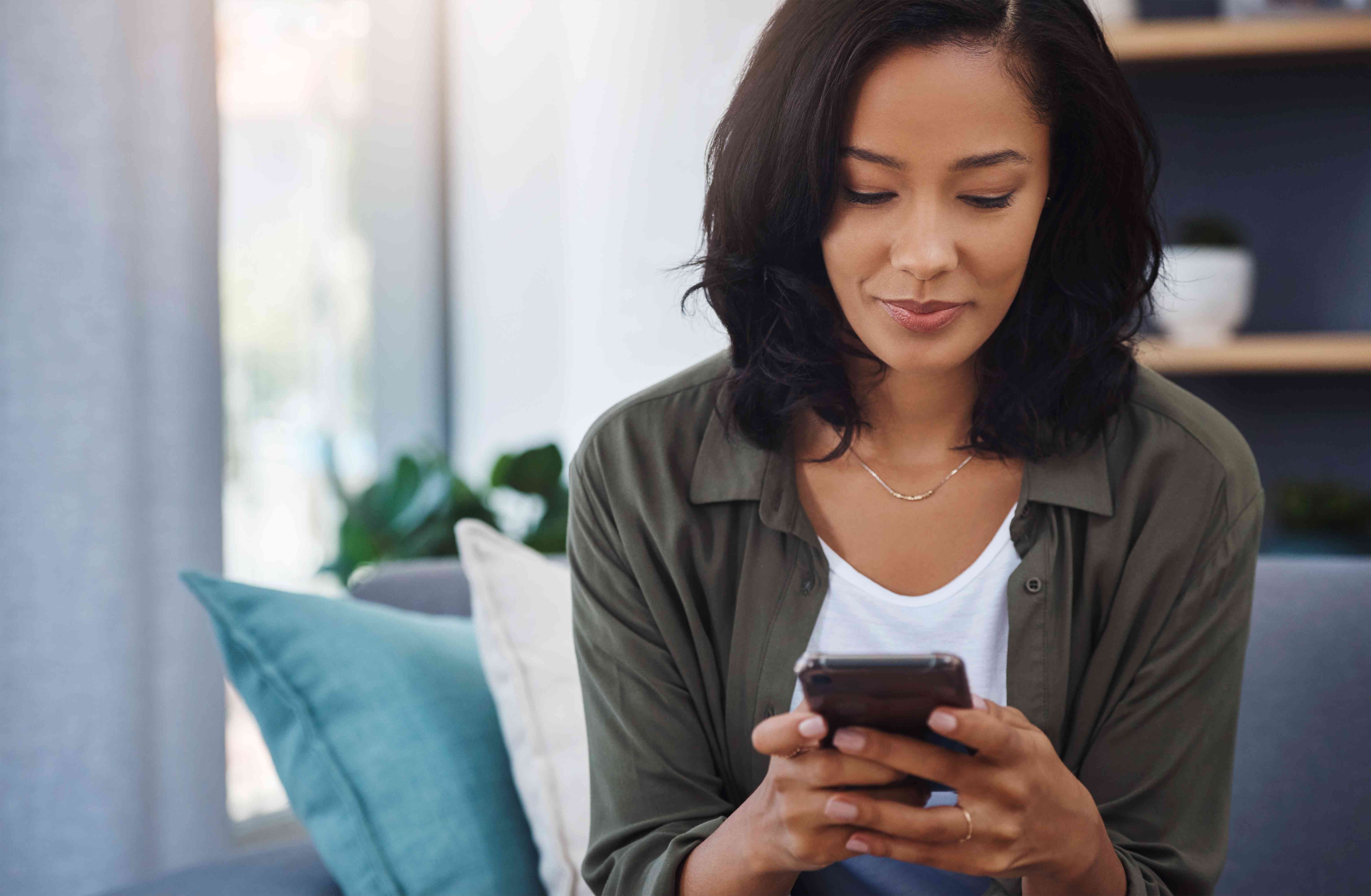 Young woman at home on couch, looking with a slight smile at something on her smartphone