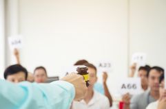 Auctioneer Pointing Gavel at Crowd of Bidders