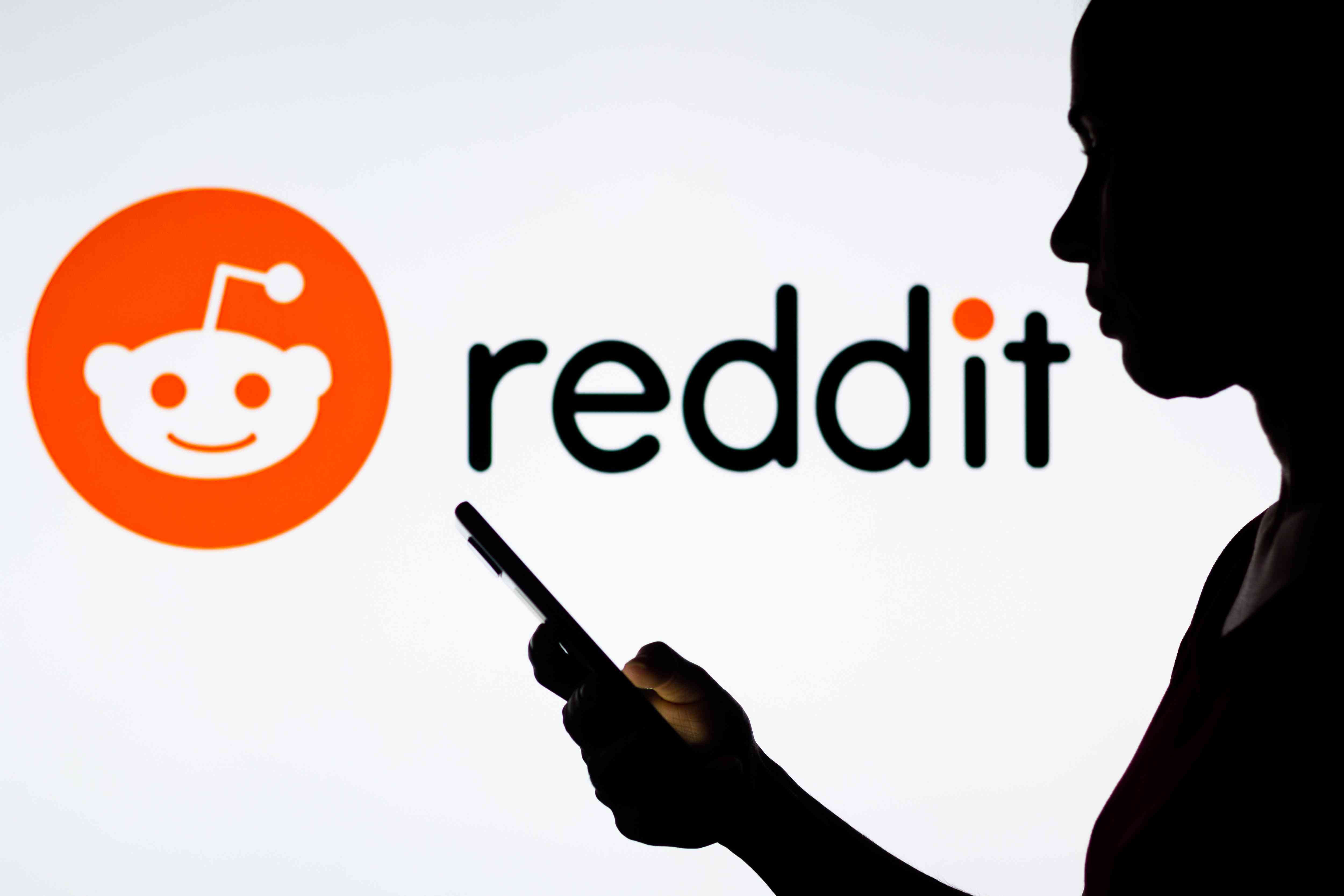 A person hold a phone in front of the Reddit logo.