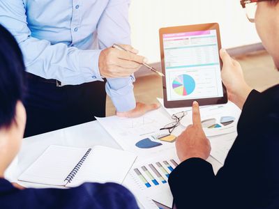 Businessman points to tablet graphic in meeting with colleagues