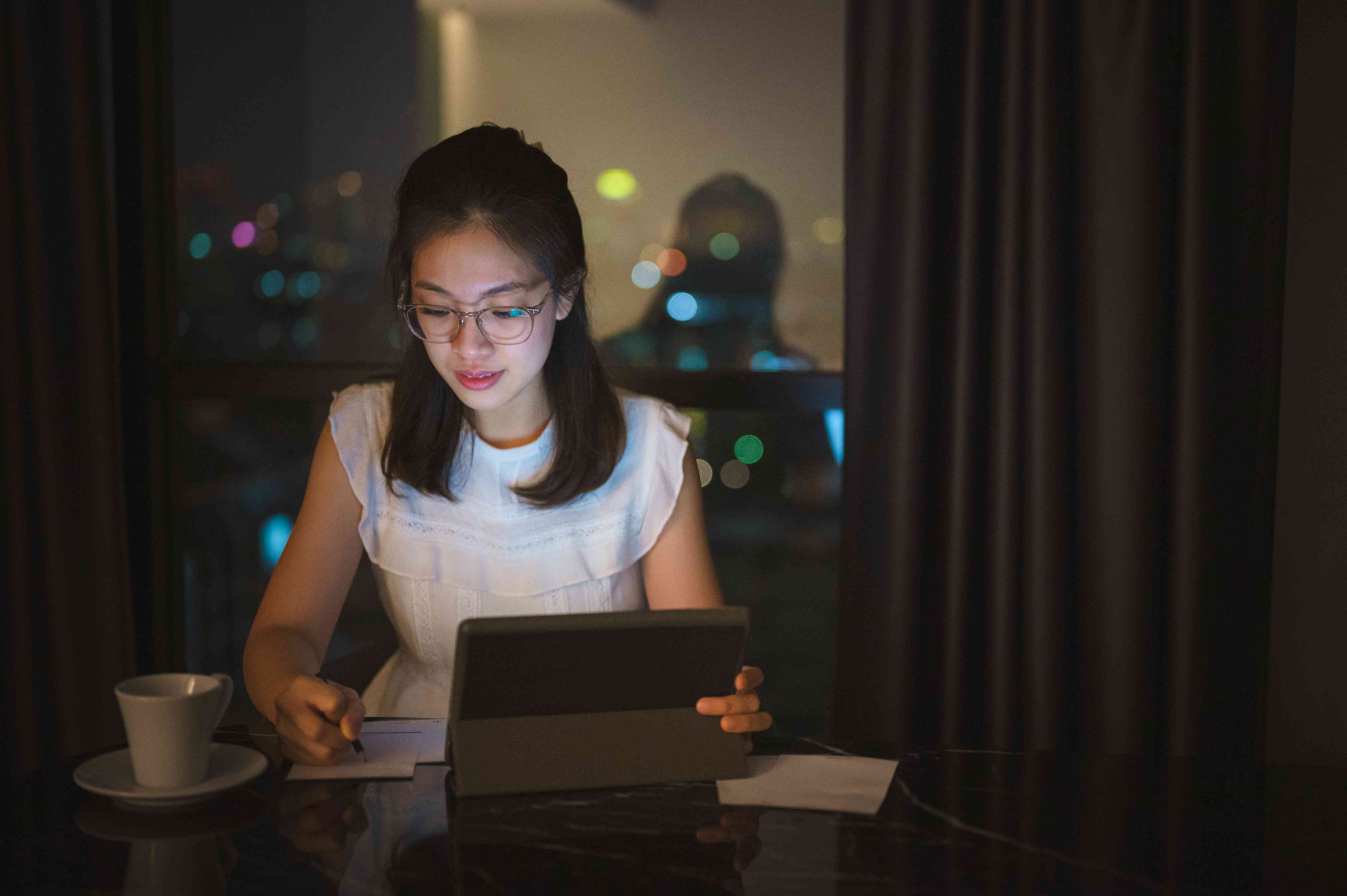 A young investor sits at a table with a laptop and a cup of coffee as they work late into the night to trade cryptocurrency.