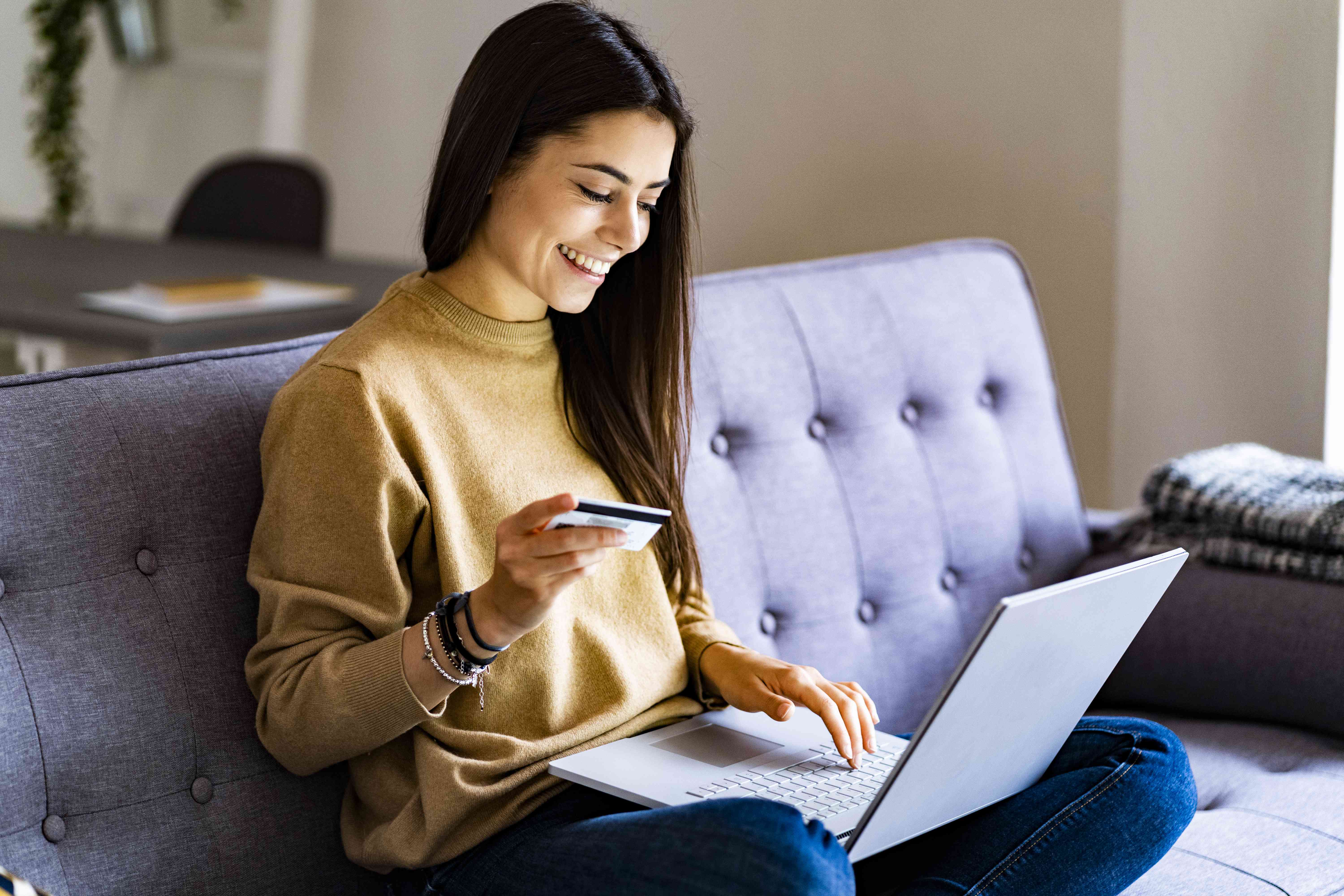 A woman on the couch uses a credit card and laptop.