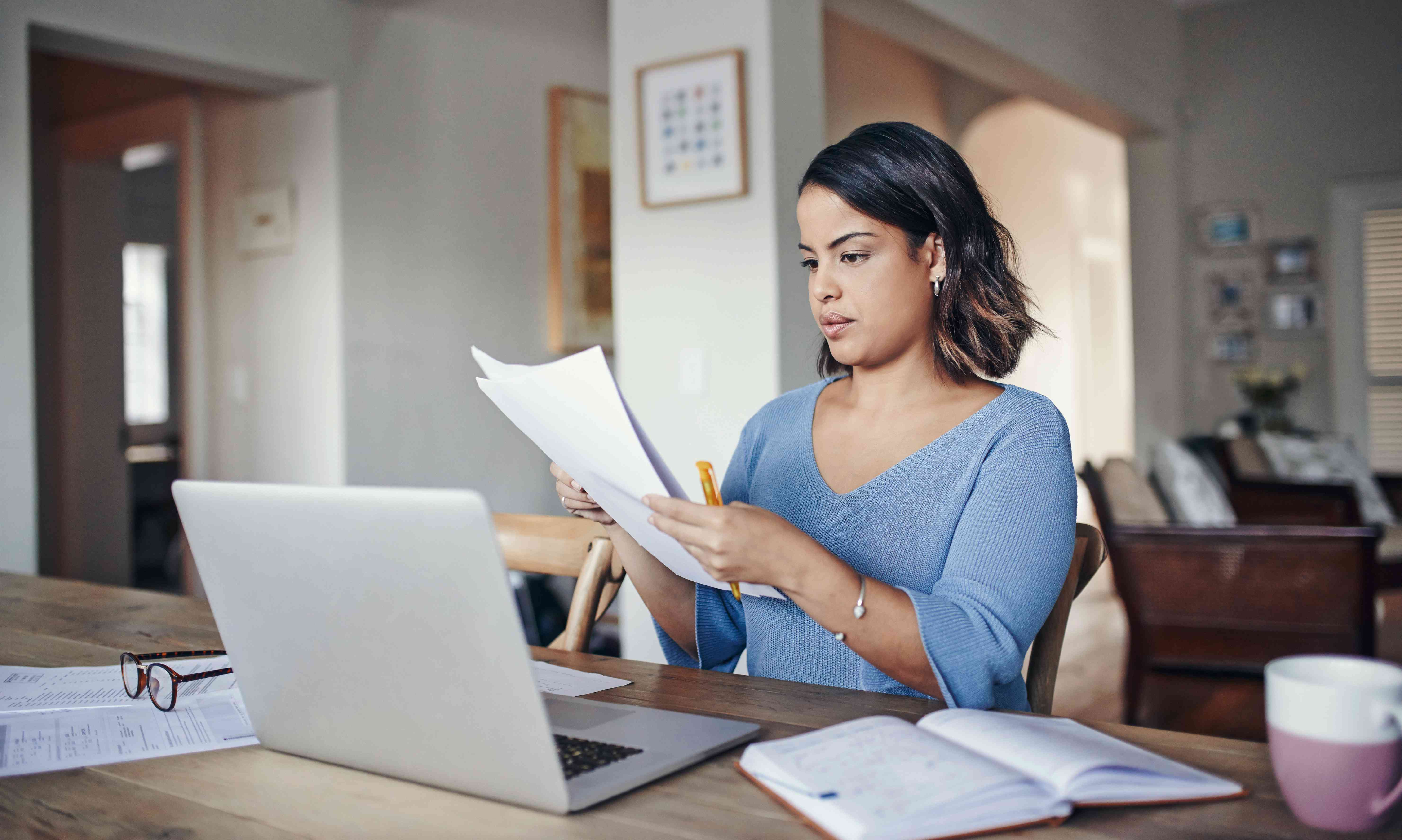 Student using laptop while going through papers about why student loan rates are so high.