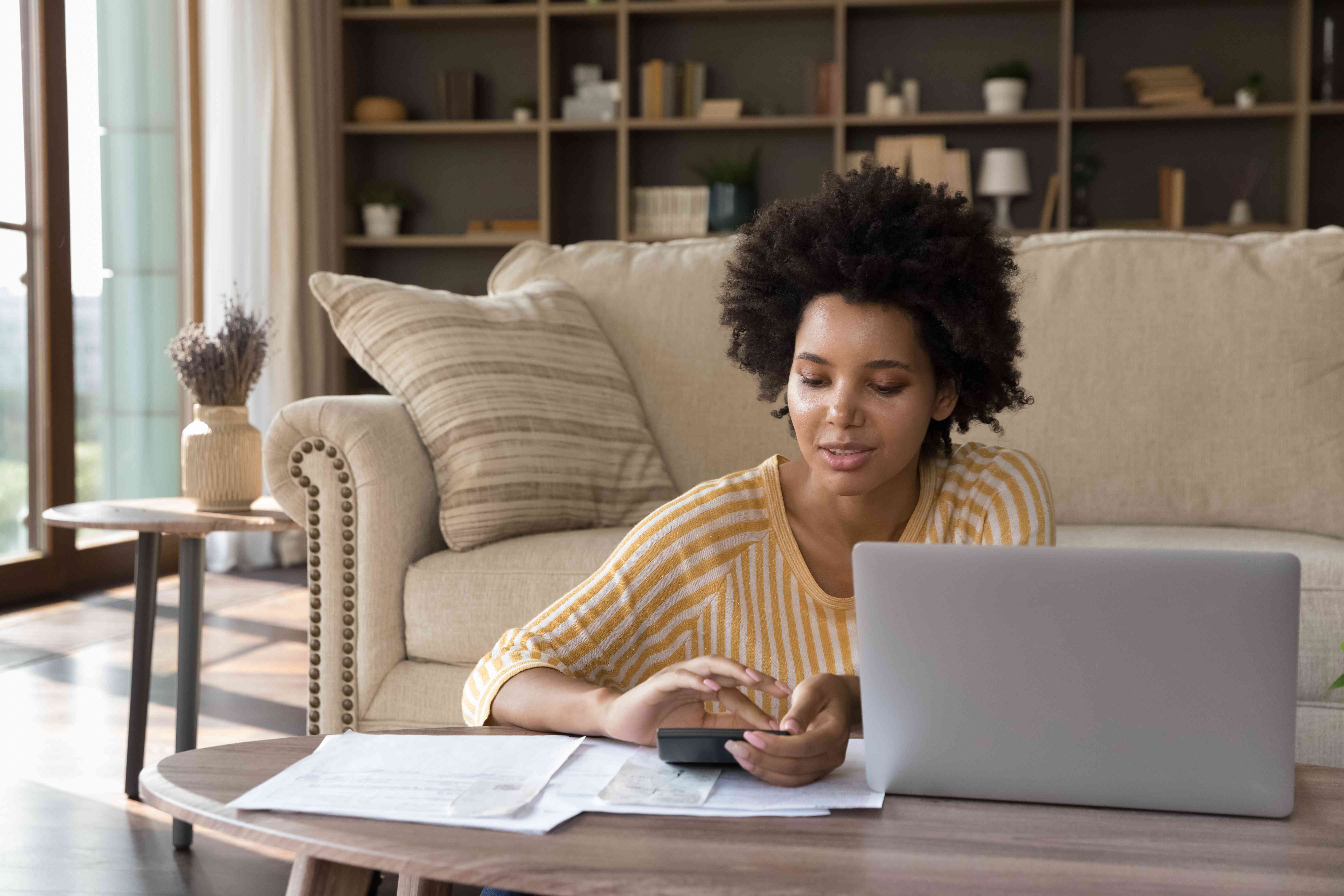 A woman sits at a low table, looking at her phone with paperwork nearby.