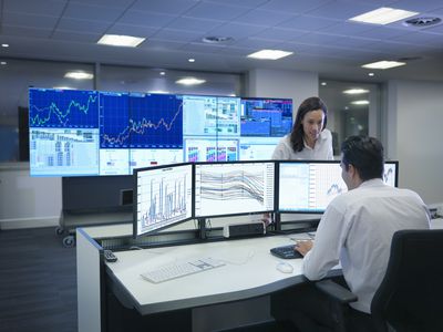 Financial analysts in an office with multiple computer monitors displaying charts and other data.