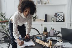 Freelancer standing at her desk, using calculator, taking notes