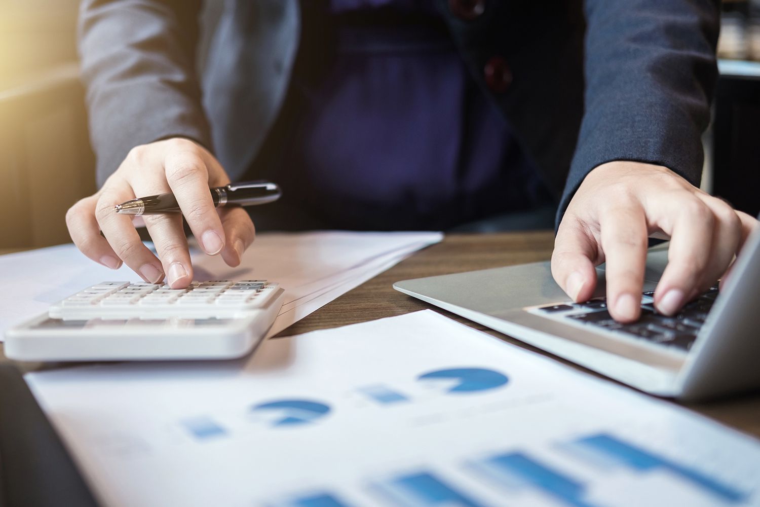 The Midsection of Businessman Using Calculator and Laptop at Desk