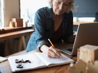 A worker makes notes with a notebook and laptop as she plans for retirement. 