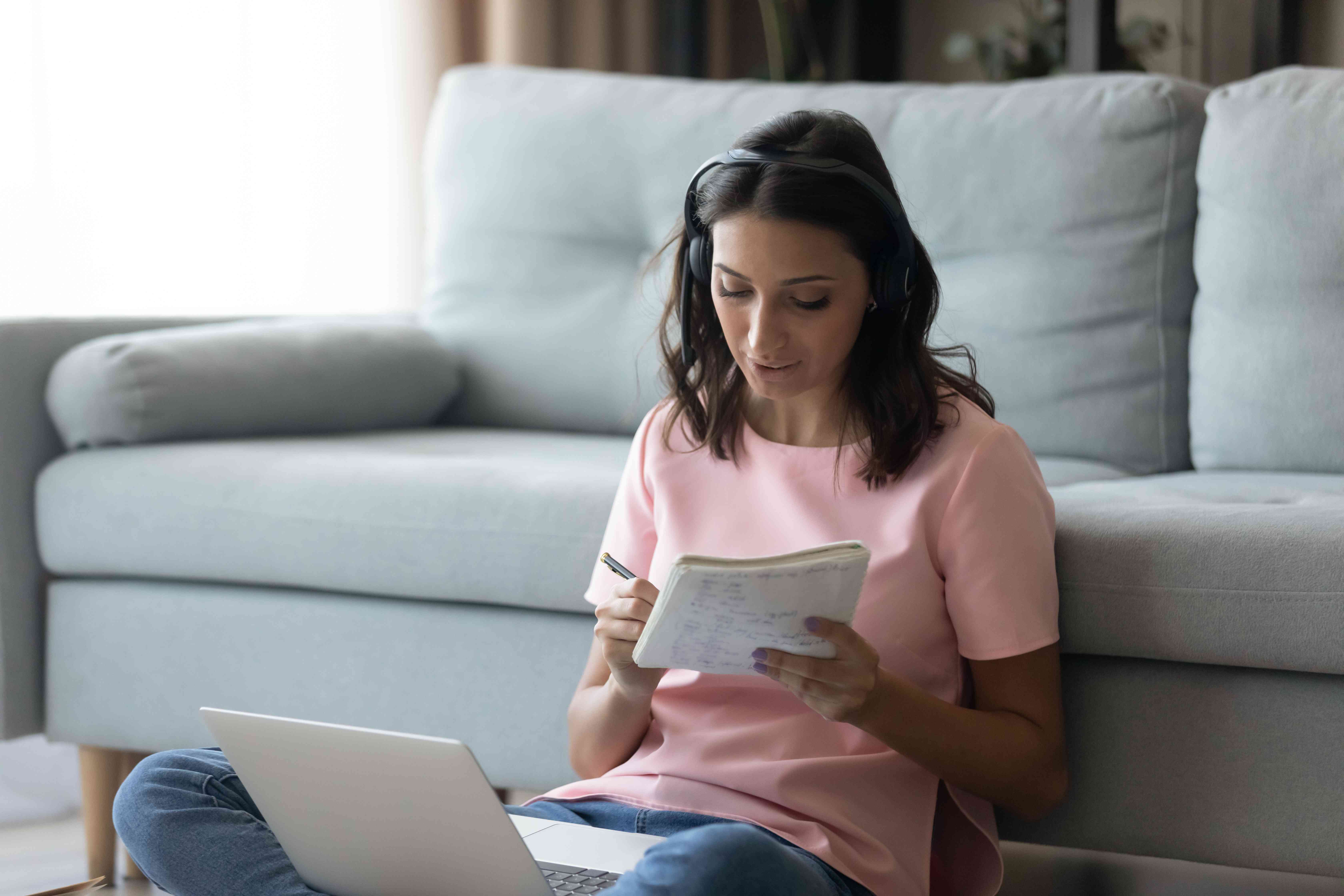 Woman sitting on the floor while making notes to compare different insurance companies based on their NAIC complaint index showing on the laptop. 